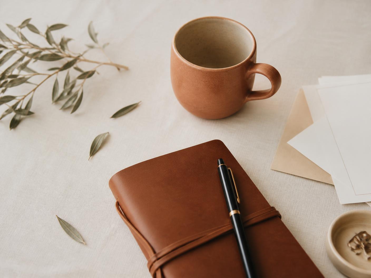 A small business owner's desk with notebook, invoices and a terracotta mug